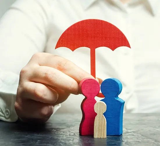 Hand holding a red umbrella over wooden figures of a family