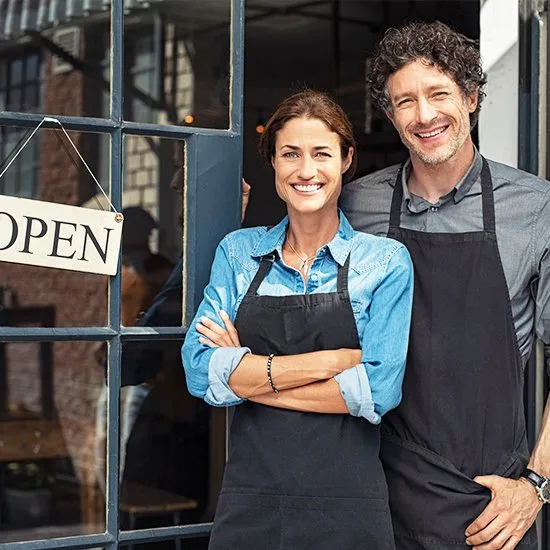 Two small business owners smiling at the open door of their shop