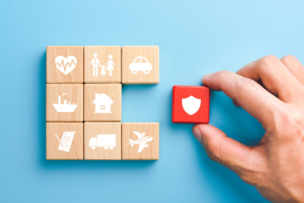 Hand holding red wooden blocks with family, life, car, travel, health and house insurance icons